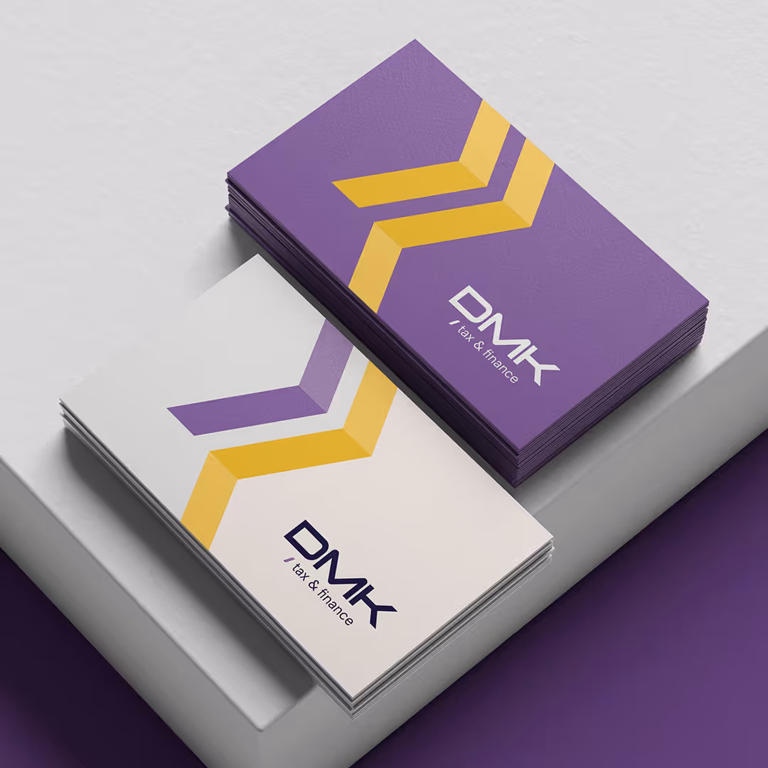 Purple and white DMK Tax & Finance business card mockups stacked on a two-tone surface, featuring the brand's yellow and purple chevron logo.